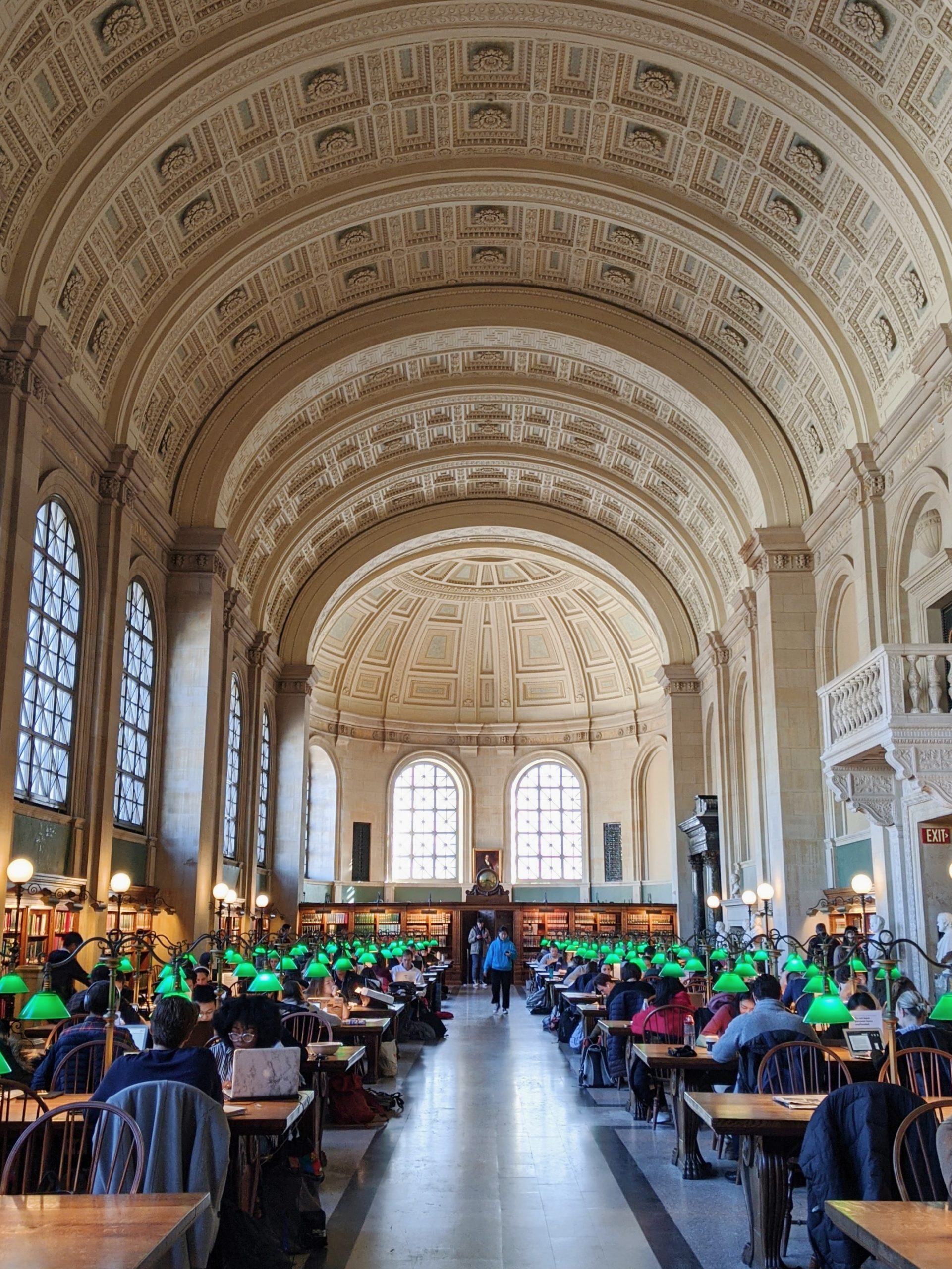 Boston public library main reading room with grand arched ceiling and rows of tables with iconic green lamps