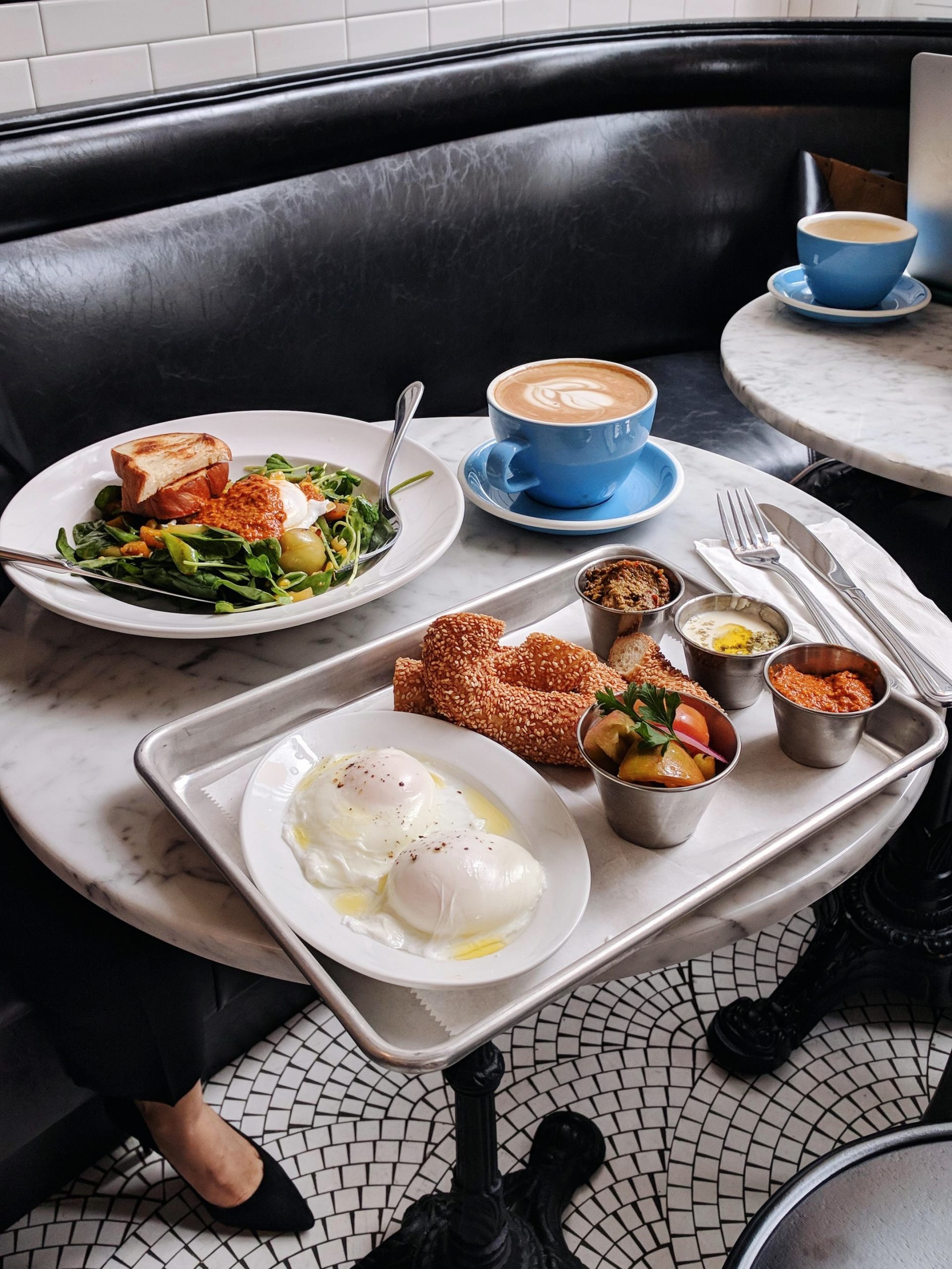 Flatlay of a tray of food, a coffee, and a plate of salad on a white marble table