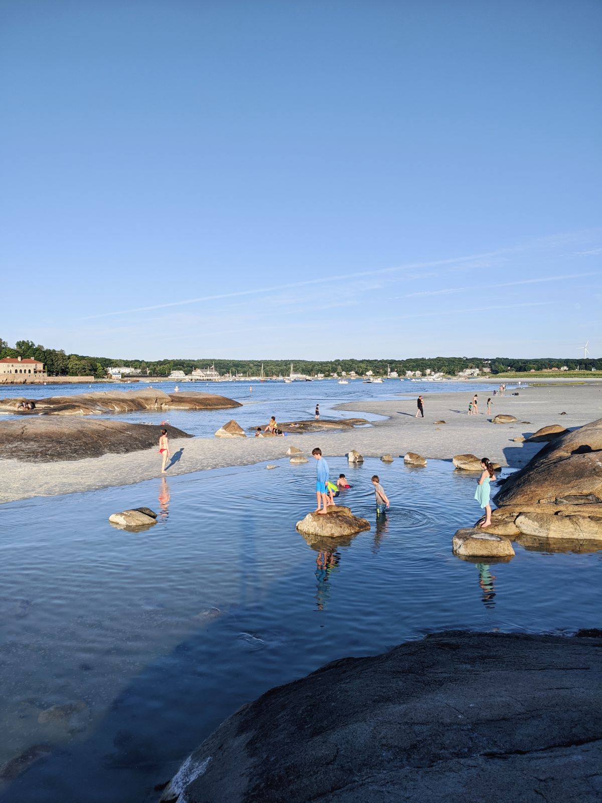 The exposed rocks of Wingaersheek Beach at low tide, with kids and adults wading in the water