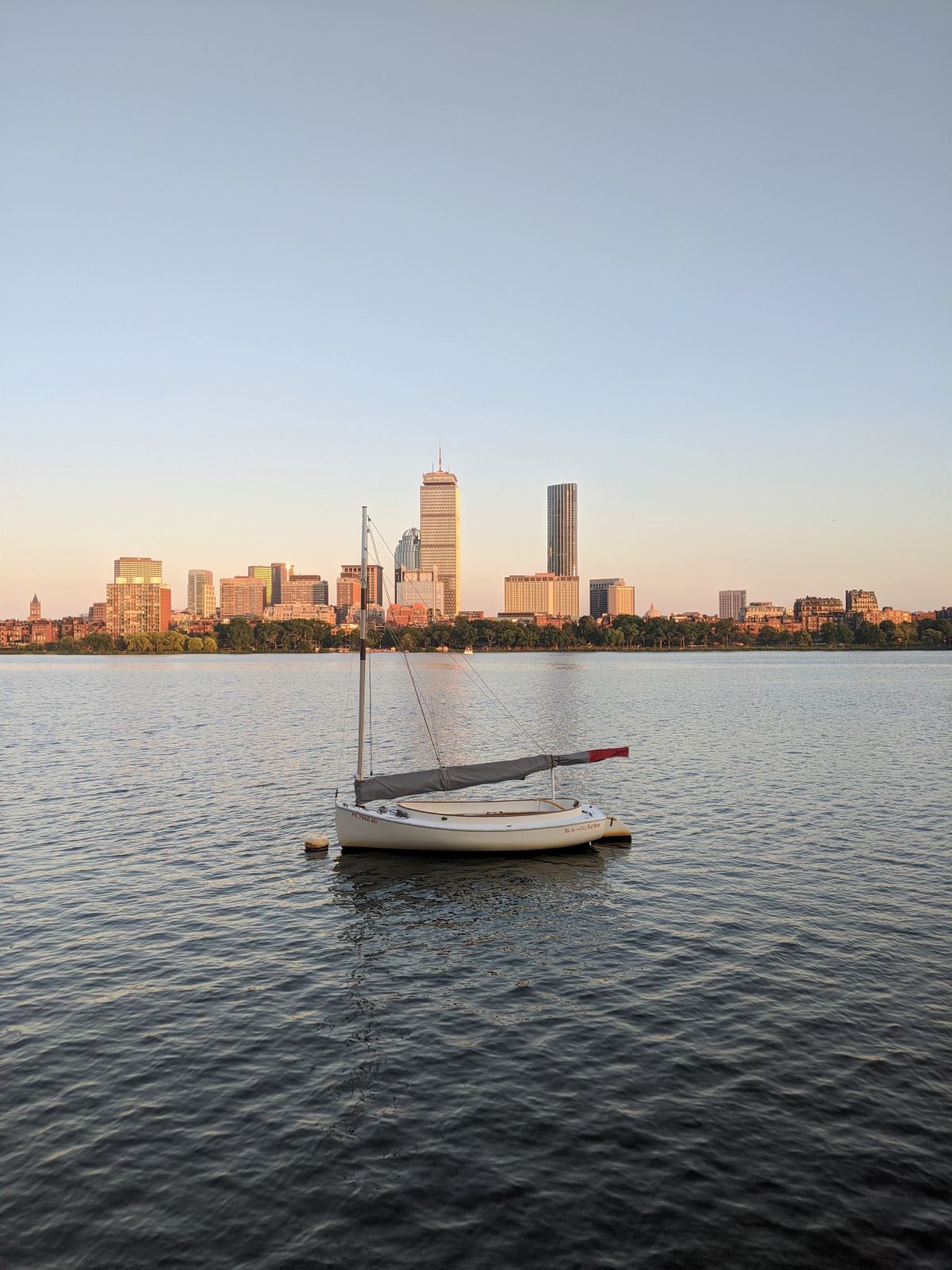 a sailboat on the Charles River with the Boston skyline in the background at sunset