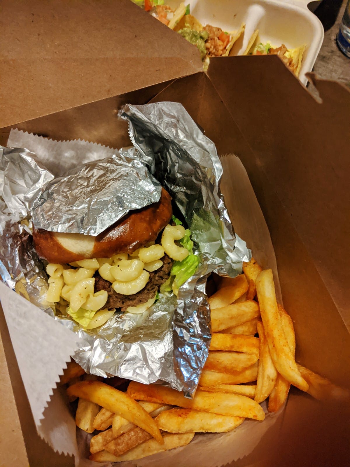 a burger with mac n cheese in a takeout box with fries